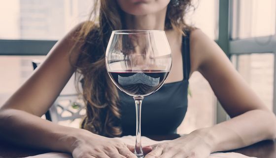 Junge Frau, sitzt vor einem großen Glas Rotwein.