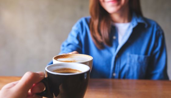 Mann und Frau, stoßen gemeinsam mit einer Tasse Kaffee an.